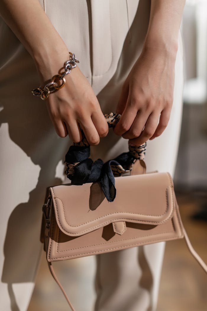 Close-up of hands holding a fashionable beige handbag with bracelets, stylish and elegant.